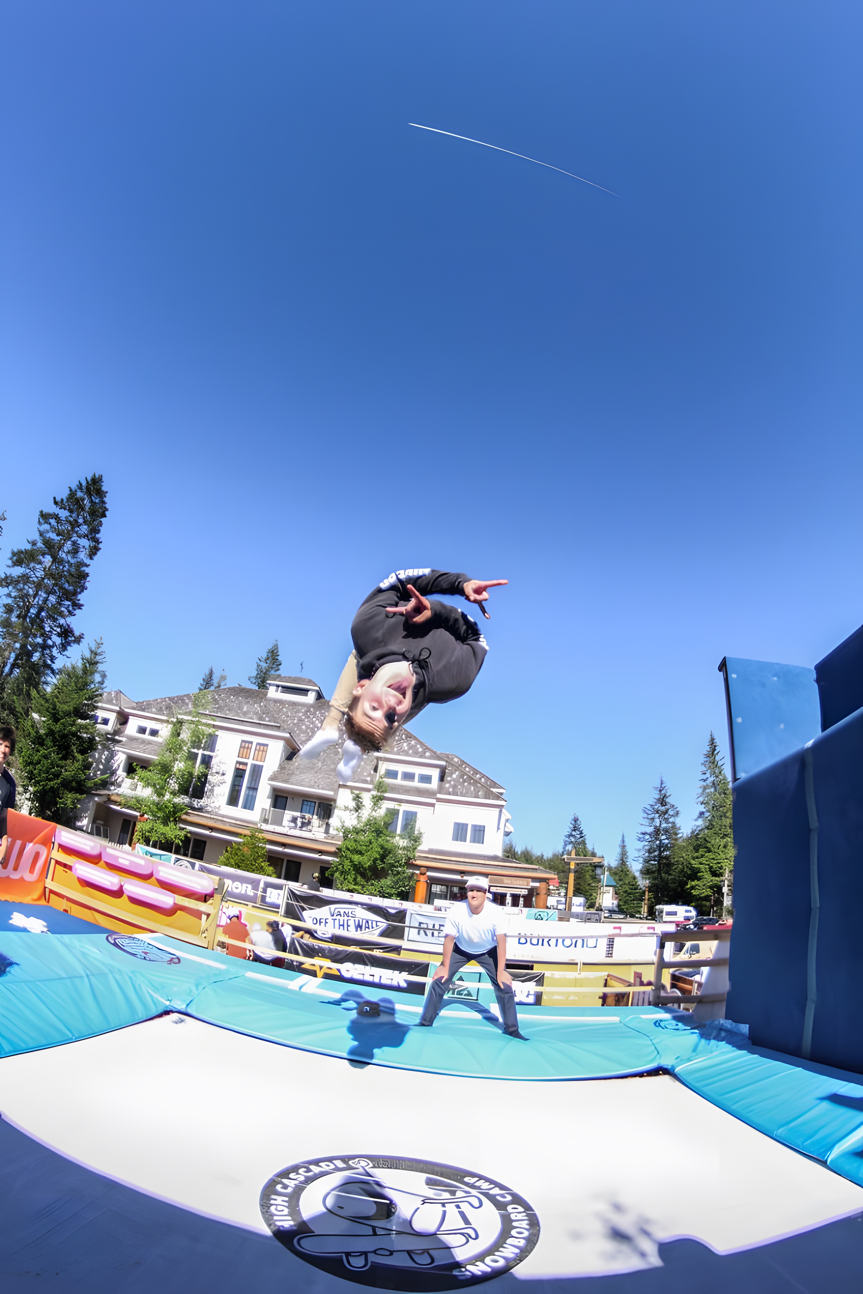 A snowboarder flipping upside down high in a clear sky above a large mountain lodge